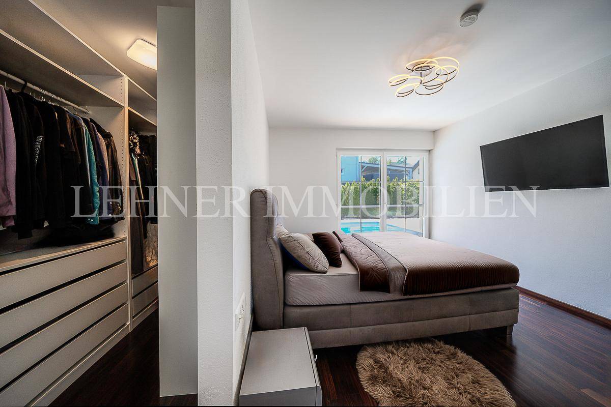 Schlafzimmer mit Holzboden, großem Bett und angrenzendem begehbarem Kleiderschrank.