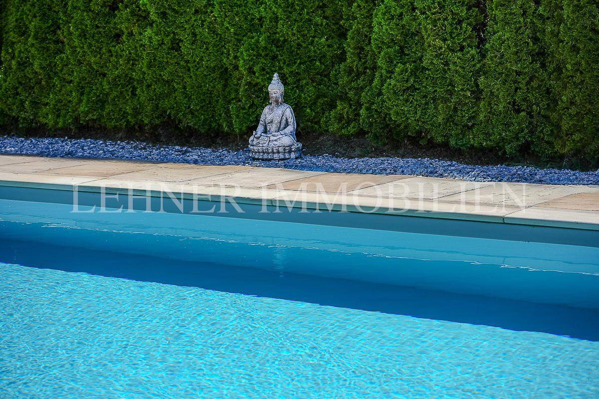 Blauer Swimmingpool im Gartenbereich mit Buddha-Statue und grüner Hecke.