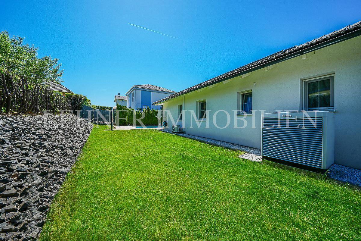 Seitlicher Gartenbereich mit Rasenfläche und moderner Wärmepumpe an der Hauswand.