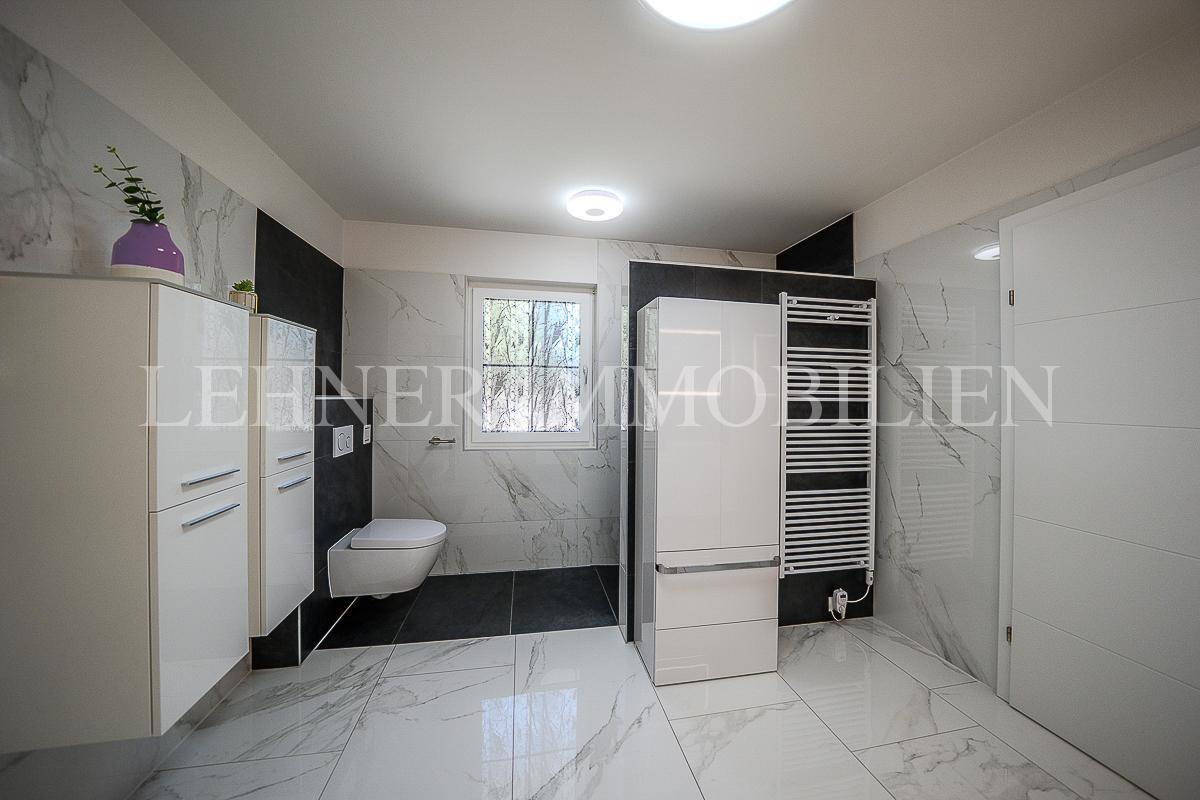 Helles Badezimmer mit WC, Fenster, beheiztem Handtuchhalter und modernen Marmorfliesen.