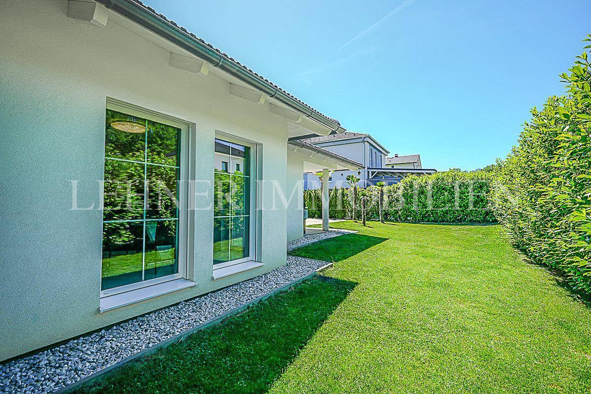 Gepflegter Rasenbereich entlang der Hausfassade mit großen Fenstern und grüner Hecke.