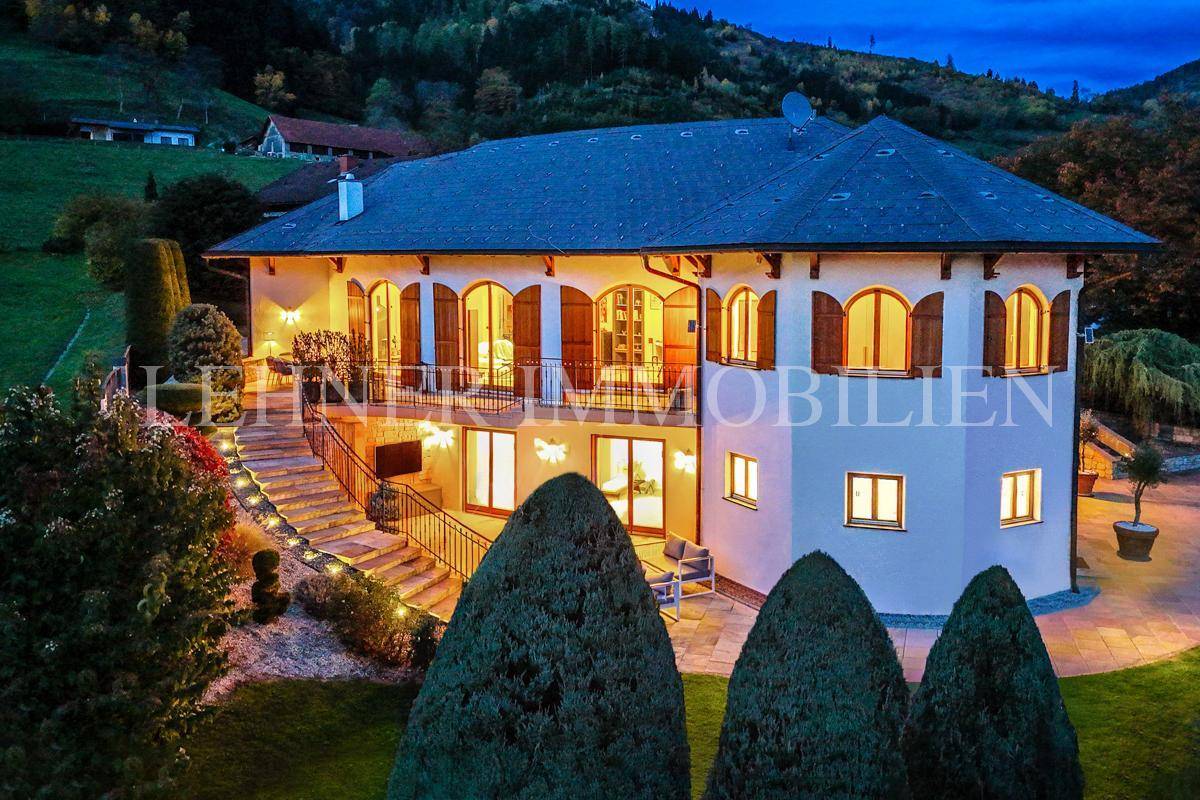Elegante Villa bei Dämmerung mit beleuchteter Terrasse und malerischem Blick auf die umliegende Landschaft.