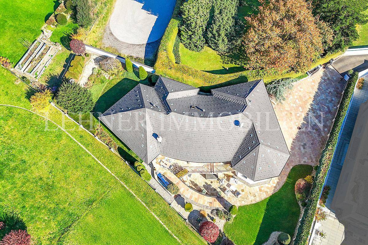 Luftaufnahme der Villa mit komplexer Dachstruktur und weitläufigem Grundstück, umgeben von viel Grün.