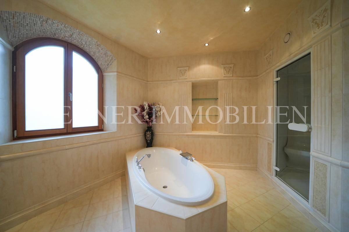 Elegantes Badezimmer mit ovaler Badewanne, hellen Fliesen und einem großen Bogenfenster.
