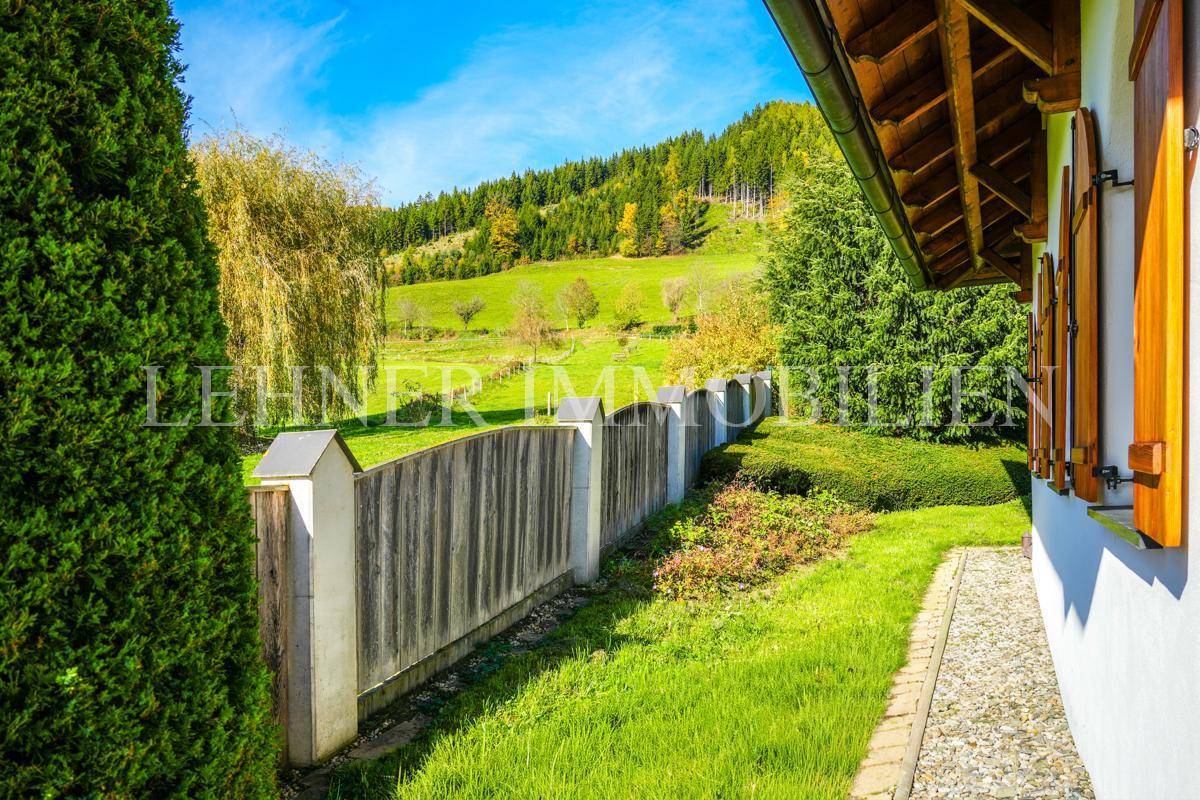 Gepflegter Gartenbereich mit Rasenfläche, Hecke und einem traditionellen Holzzaun.