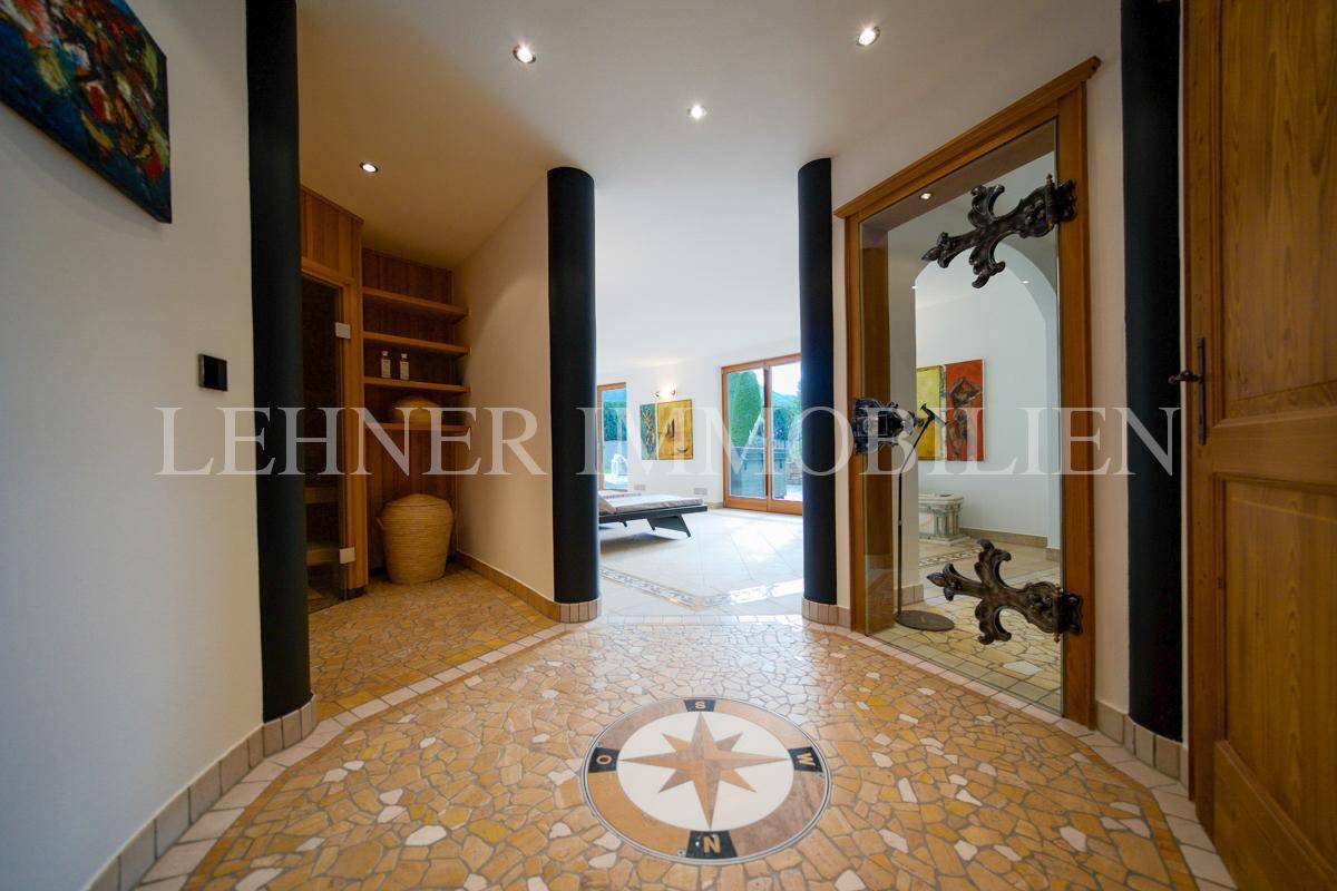 Einladender Eingangsbereich mit dekorativem Mosaikboden, Säulen und Blick auf den Wohnbereich mit großen Glastüren.