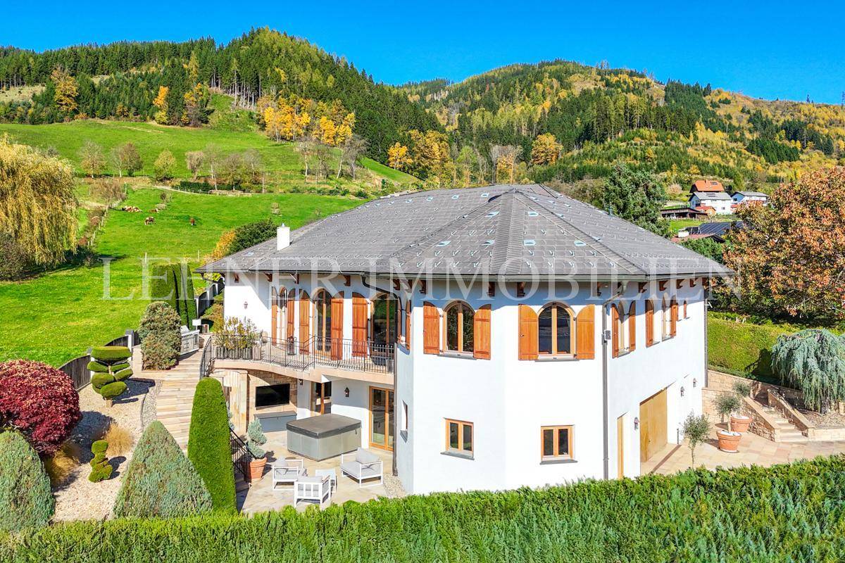 Panoramablick auf das Anwesen mit Terrasse, Whirlpool und weitläufigem Garten vor Bergkulisse.