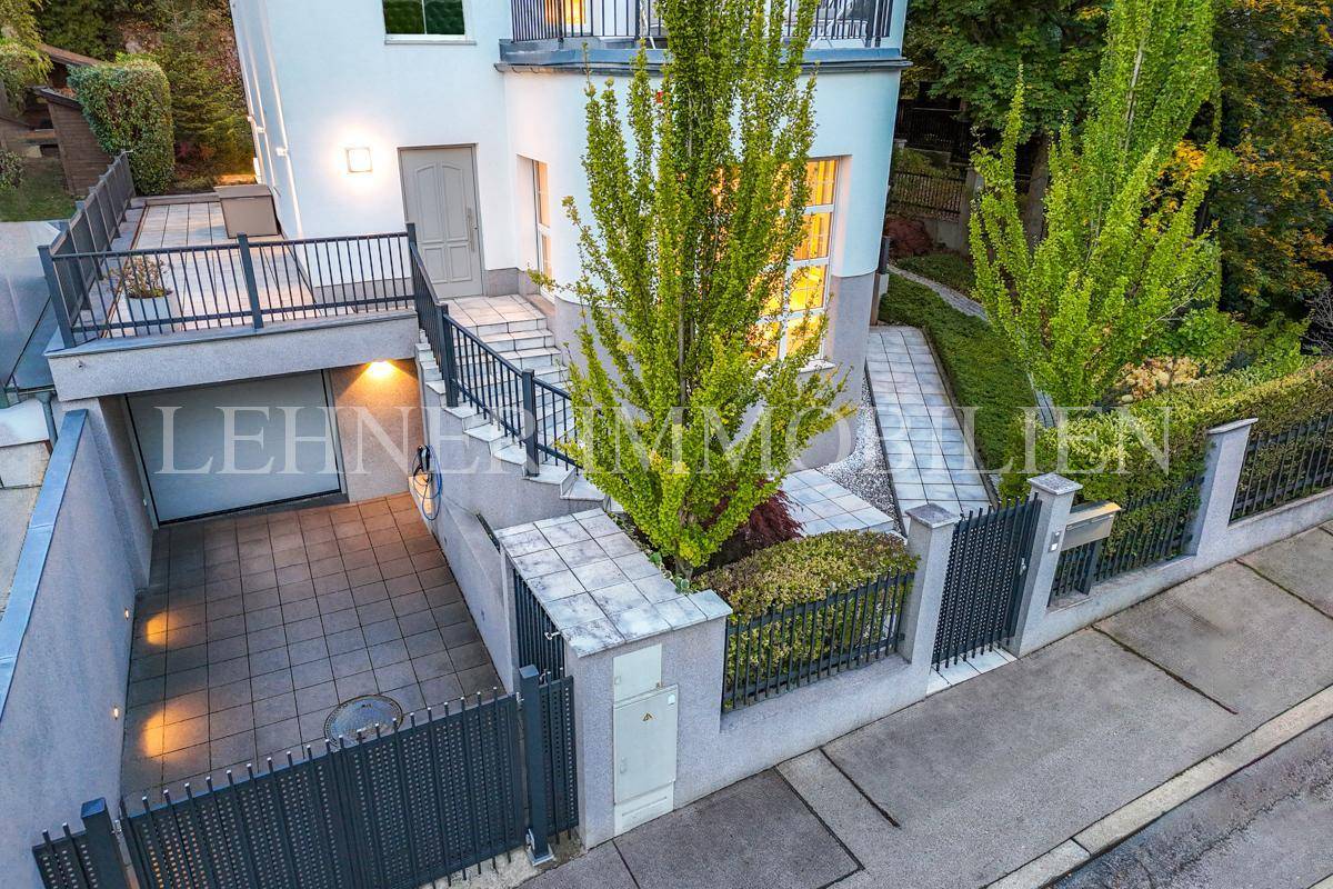 Eingangsbereich der Stadtvilla mit Garagenzufahrt, gepflastertem Vorplatz und Zaun.