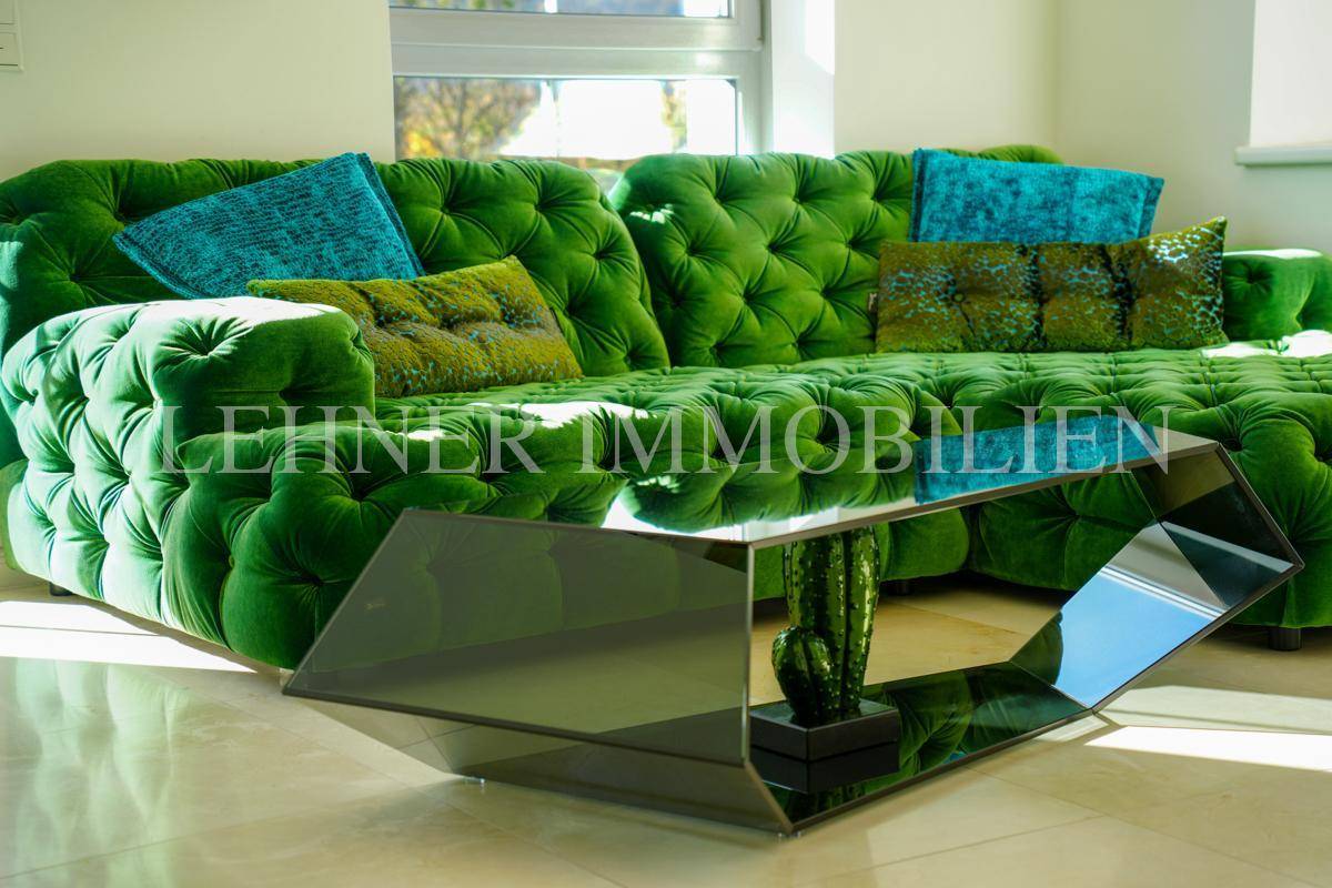 Detailaufnahme des luxuriösen grünen Sofas mit Samtbezug und des modernen Glas-Couchtisches.