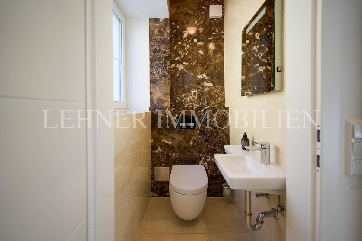 Modernes Gäste-WC mit eleganten Marmorfliesen, wandhängendem WC und kleinem Waschbecken.
