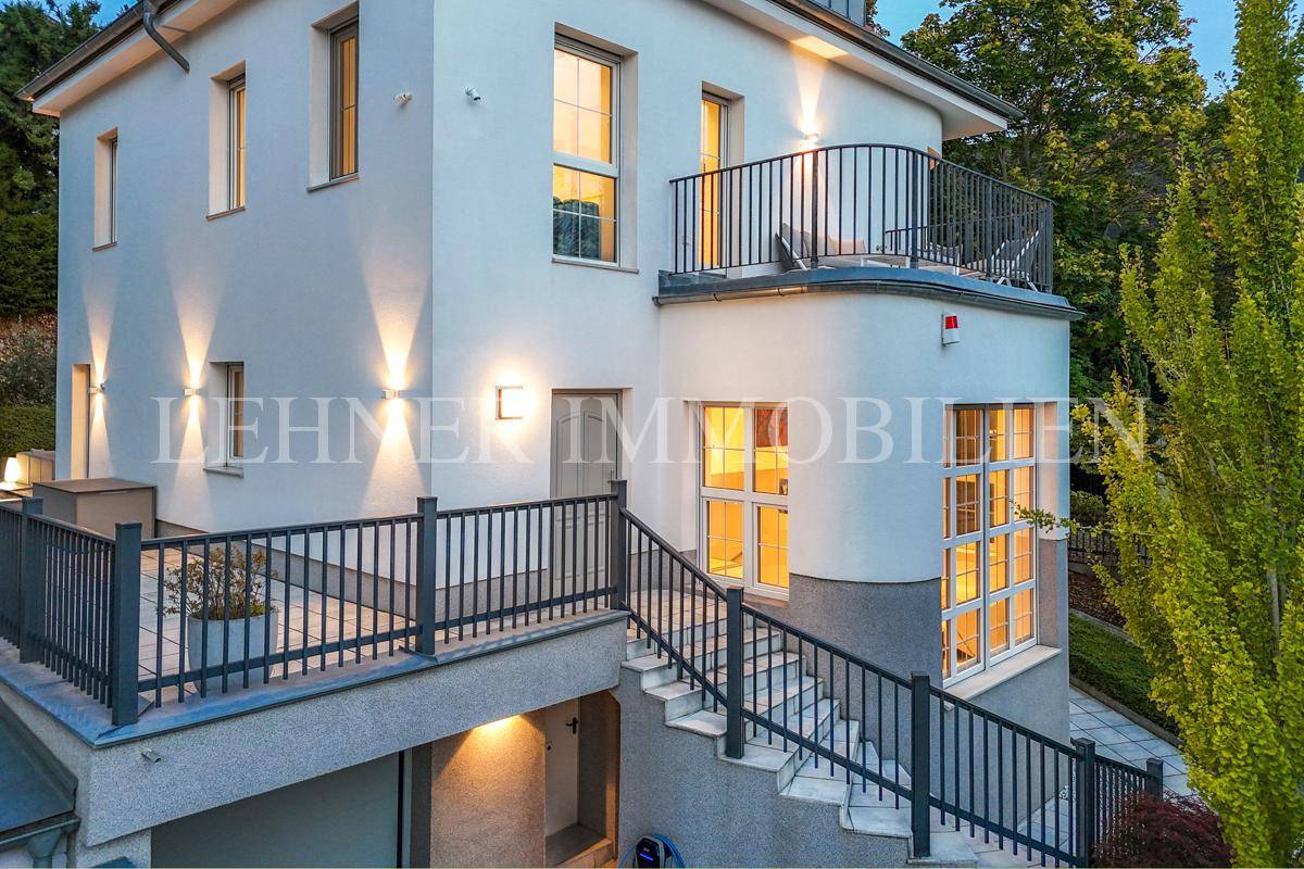 Seitliche Ansicht der beleuchteten Stadtvilla mit Treppenaufgang und Balkon bei Dämmerung.
