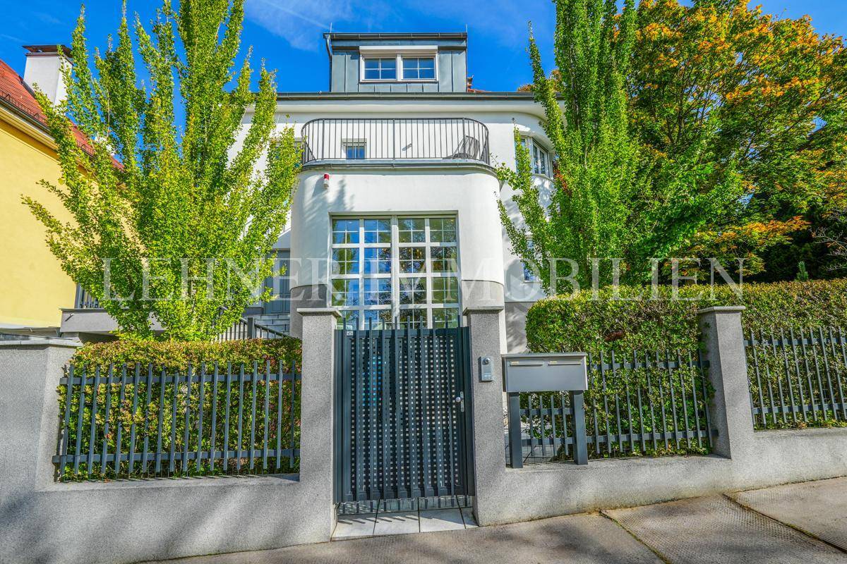 Vorderansicht der Stadtvilla mit Eingangstor, gepflegter Hecke und hohen Bäumen.