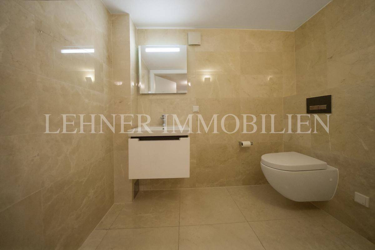 Modernes Badezimmer im Untergeschoss mit Wand-WC, Waschbecken und hellen Fliesen.