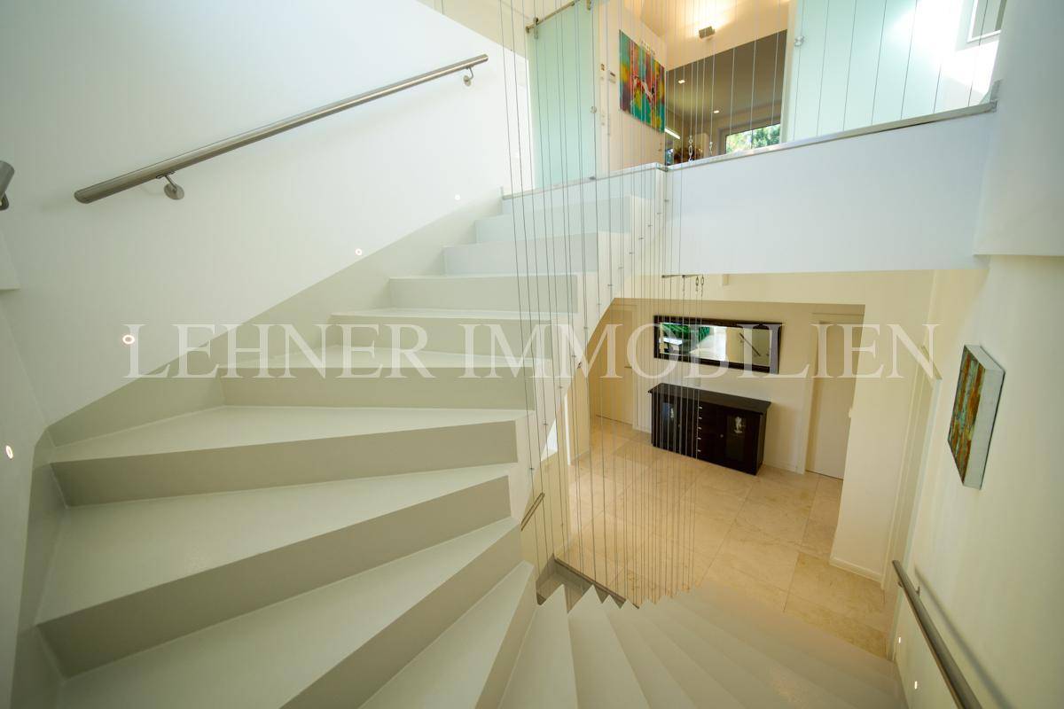 Elegante Treppe mit klaren Linien und Blick auf den unteren Flurbereich mit dunklem Sideboard.
