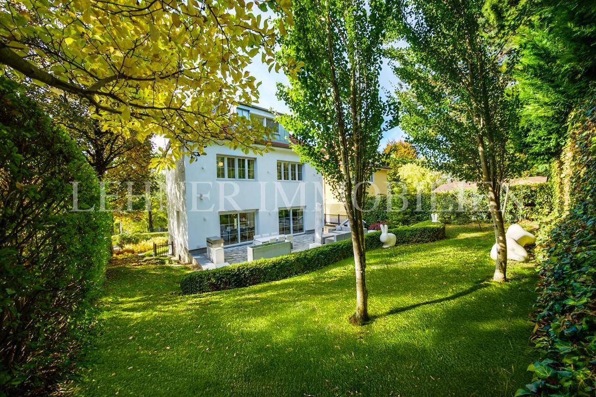 Weitläufiger Garten mit Rasenflächen, hohen Bäumen und Blick auf die moderne Villa.