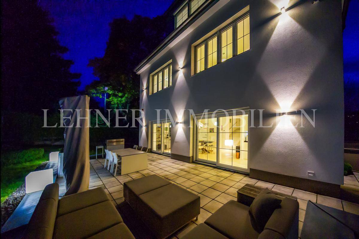 Seitlicher Blick auf die beleuchtete Terrasse mit Lounge-Möbeln und Zugang zum Haus.
