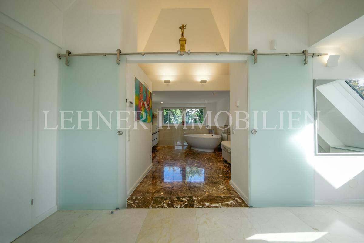 Geräumiges Badezimmer mit freistehender Badewanne und modernen Glasschiebetüren, verbunden durch Marmorboden.