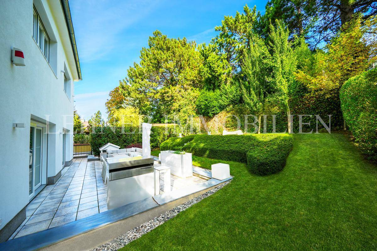 Sonnige Terrasse mit Essbereich und Lounge-Möbeln, umgeben von üppigem Grün und Rasen.