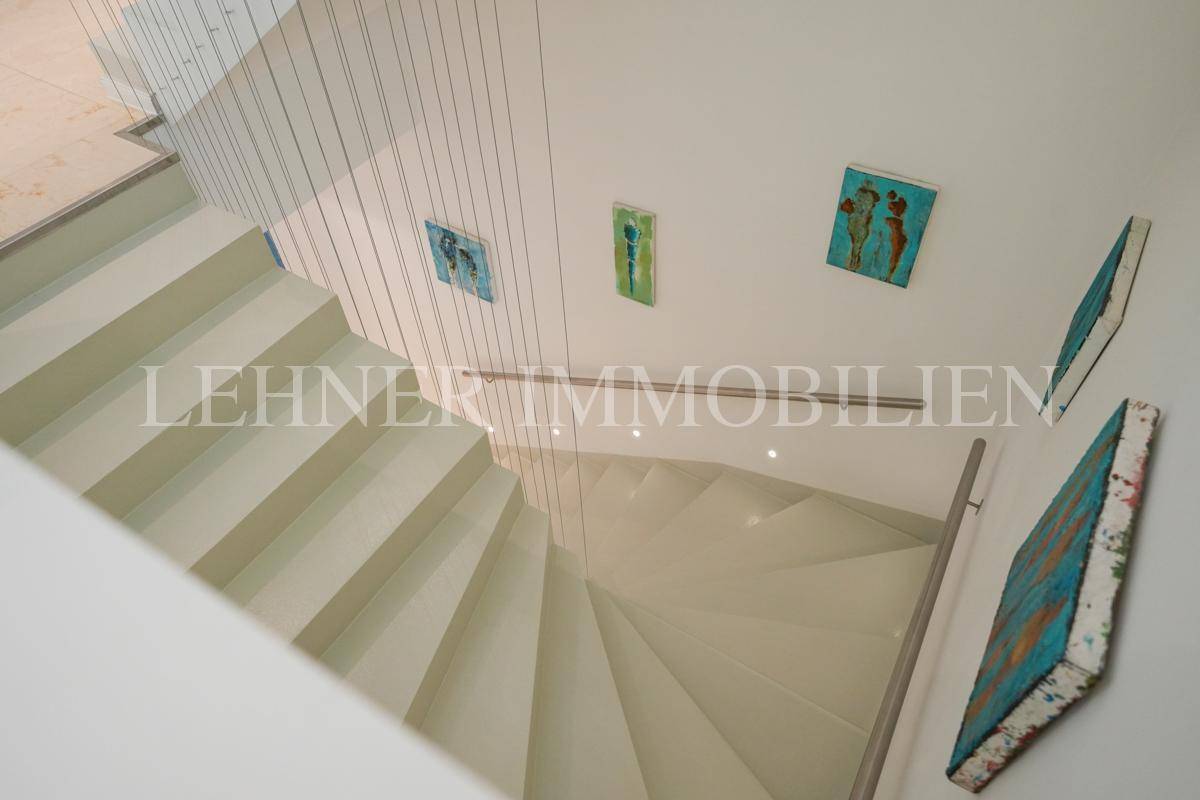 Moderne Treppe mit schwebenden Stufen und filigranem Seilgeländer, geschmückt mit farbigen Kunstwerken.