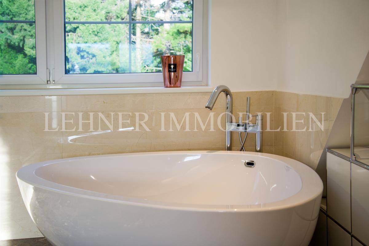 Detailaufnahme der freistehenden Badewanne mit modernem Wasserhahn und Fensterblick ins Grüne.