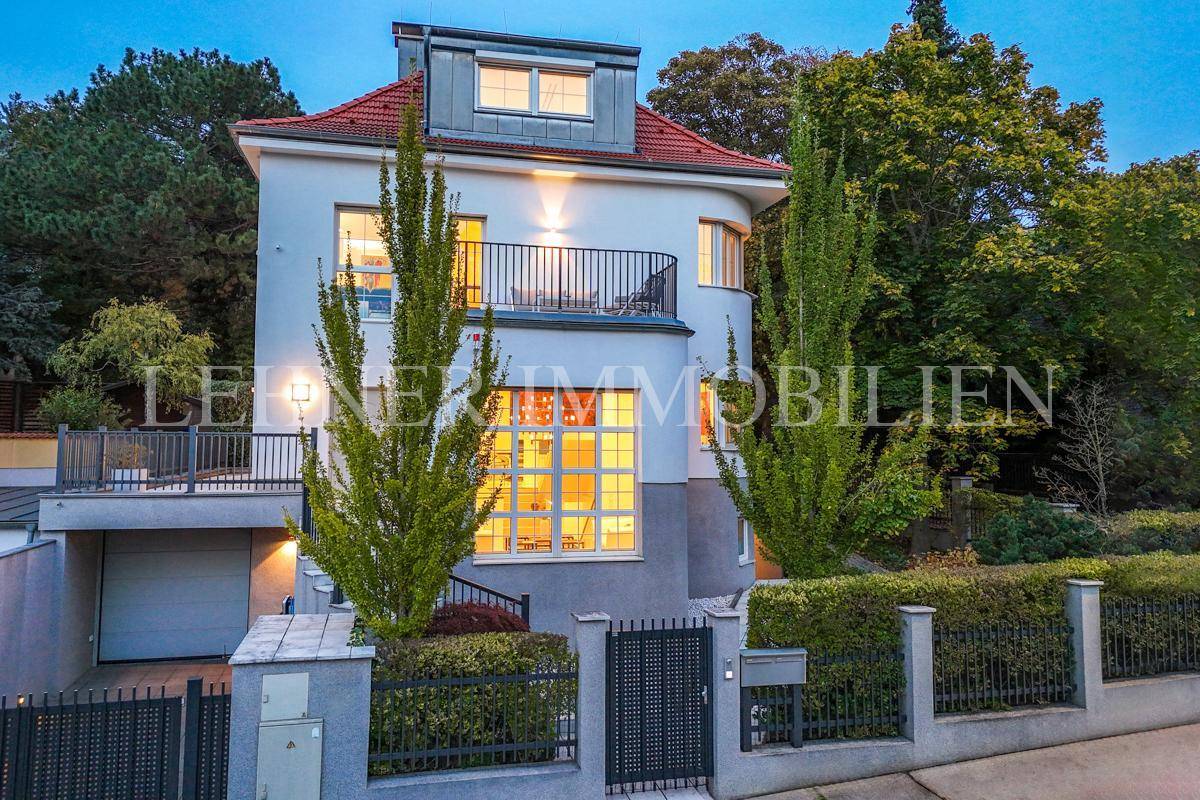 Die Stadtvilla bei Nacht, umgeben von Bäumen, mit beleuchtetem Eingangsbereich und Balkon.
