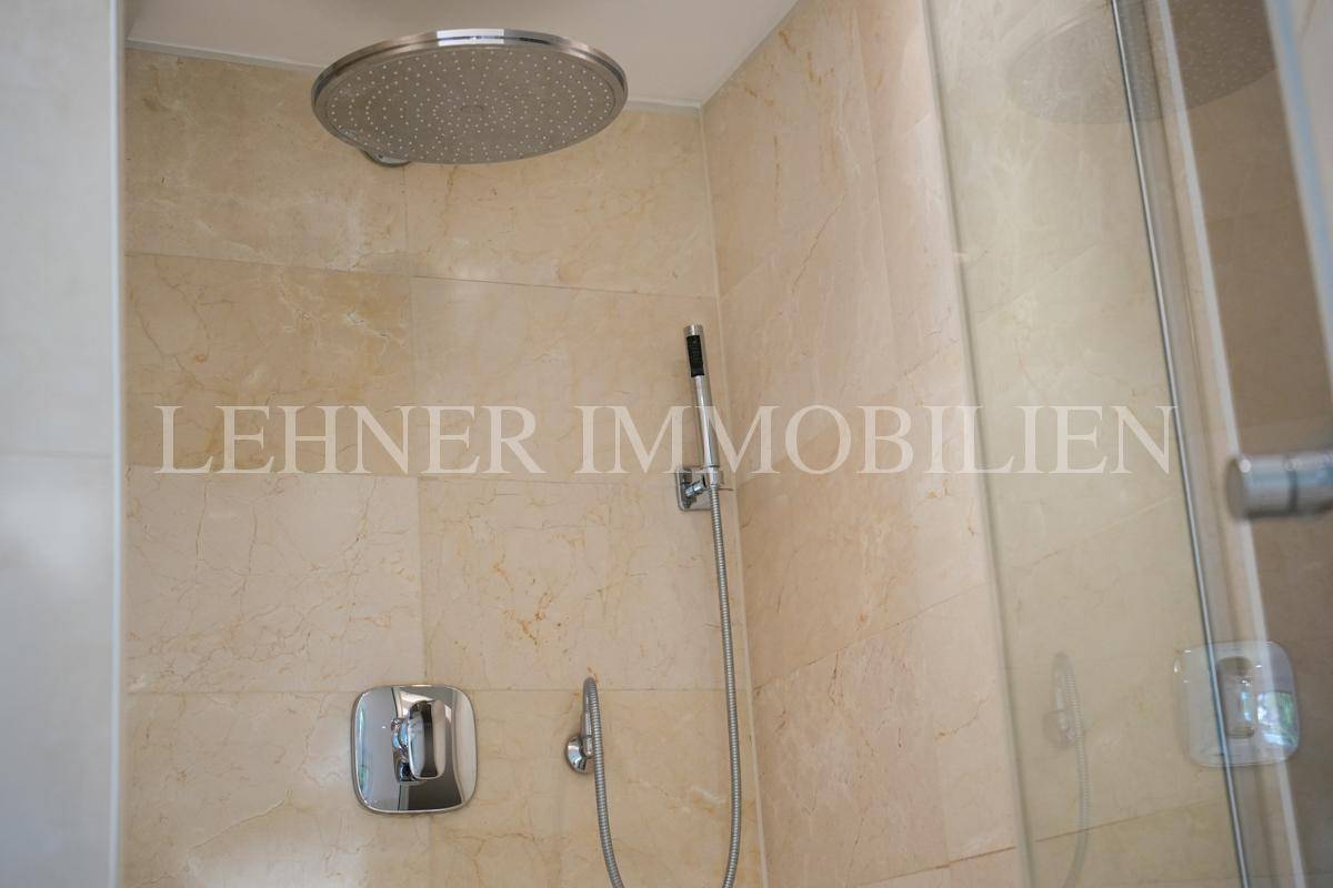 Detailansicht der modernen Regendusche mit großem Duschkopf und hellen Fliesen im Badezimmer.