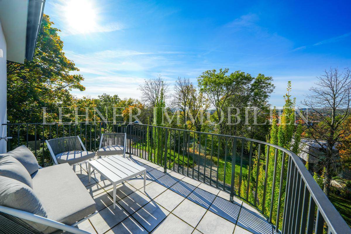 Sonniger Balkon mit modernen Gartenmöbeln und weitem Blick über grüne Bäume und die Umgebung.