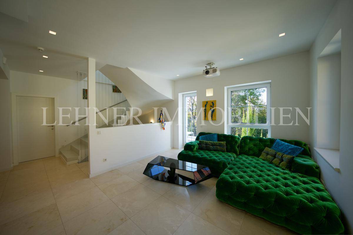Großzügiges Wohnzimmer mit markantem grünem Sofa, Projektor und Zugang zum Treppenbereich.