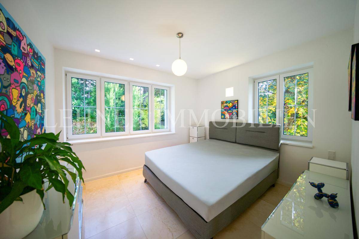 Helles Schlafzimmer mit Doppelbett, farbenfroher Kunst und großen Fenstern mit Blick ins Grüne.