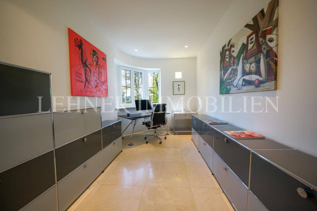 Modernes Arbeitszimmer mit großen Fenstern, viel Stauraum und künstlerischer Dekoration.