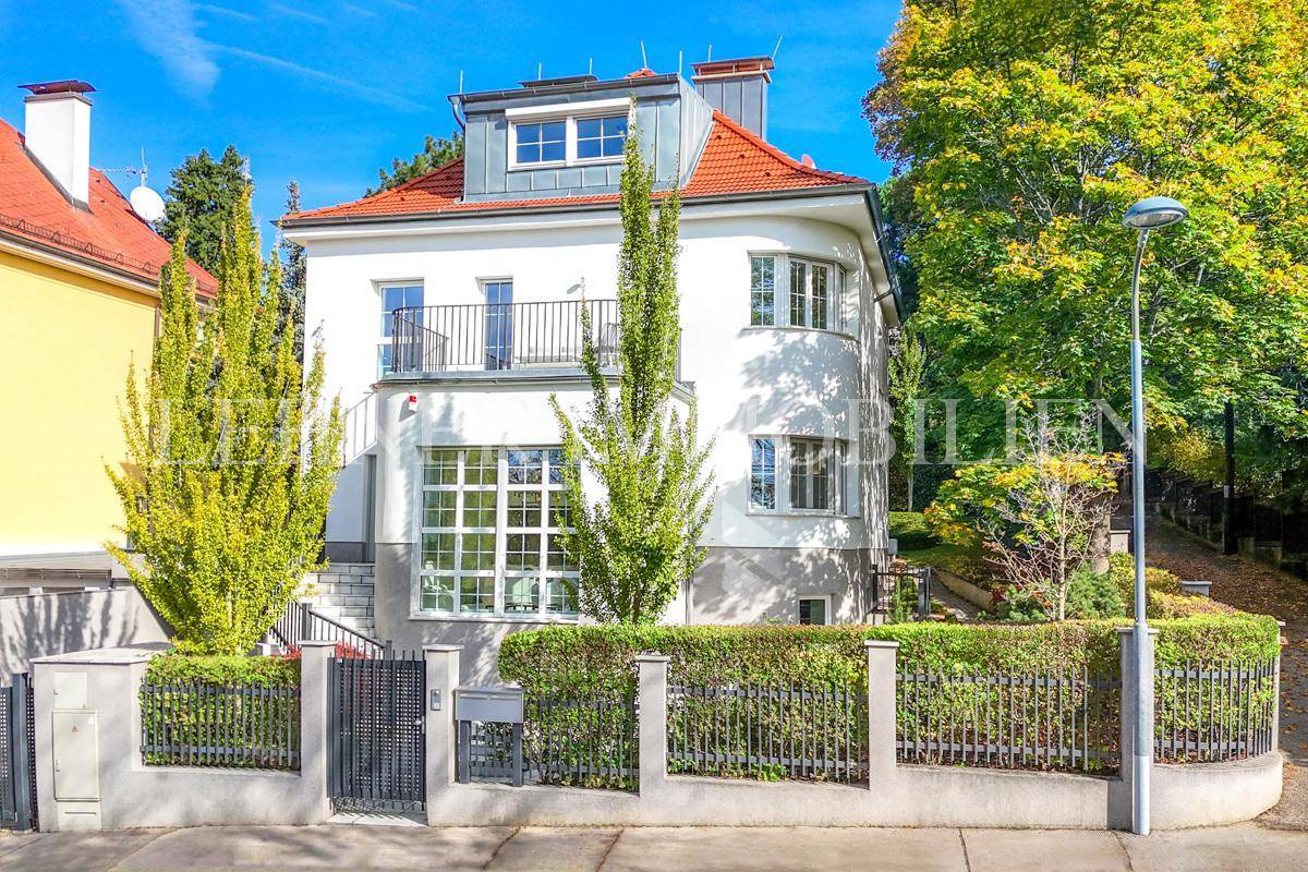 Die elegante Stadtvilla bei Tageslicht mit Balkon und üppiger grüner Umgebung.