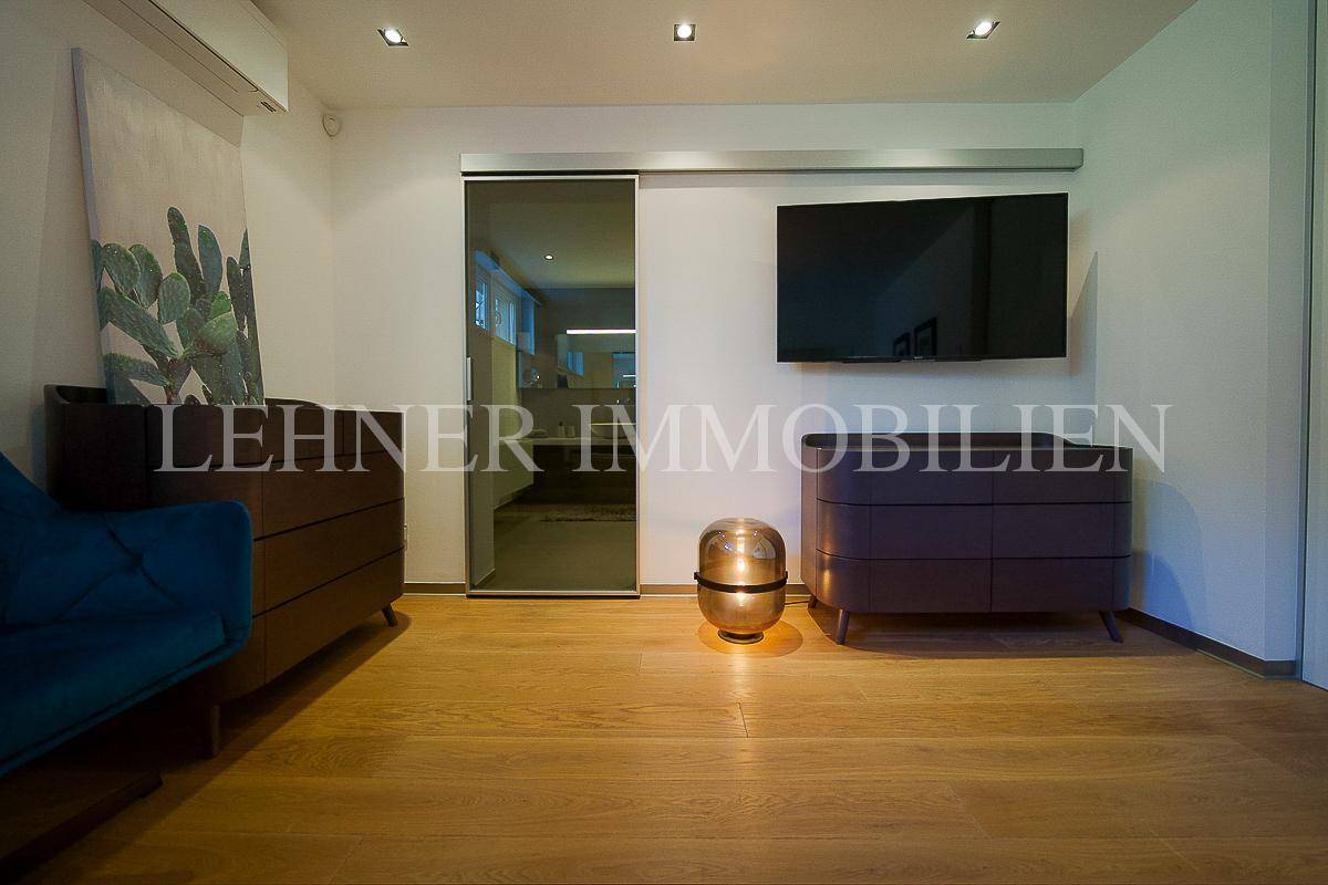 Schlafzimmer mit Kommode, Fernseher und einer Glasschiebetür, die zu einem angrenzenden Raum führt.