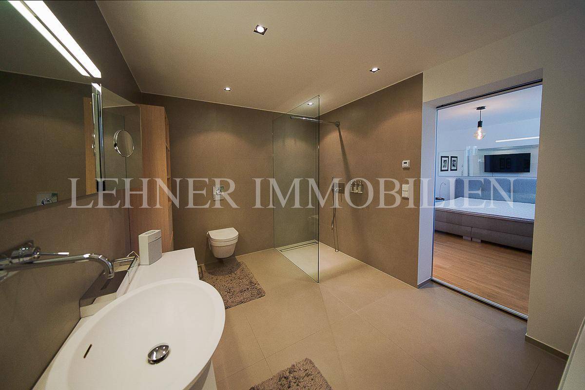 Geräumiges Badezimmer mit begehbarer Dusche und direktem Zugang zum Schlafzimmer durch eine Glastür.