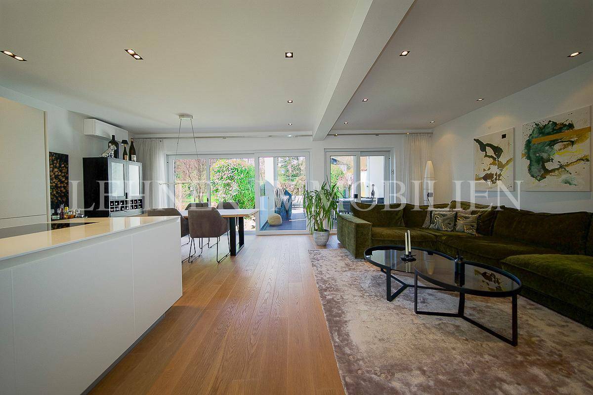Geräumiger offener Wohn- und Essbereich mit Holzboden, großer Couch und Zugang zur Terrasse.