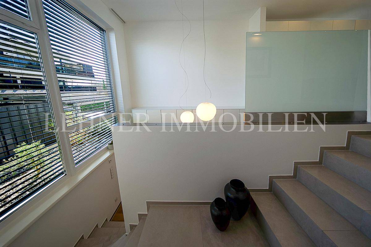 Moderner Treppenaufgang mit minimalistischer Dekoration, Glasgeländer und stilvollen Hängelampen.