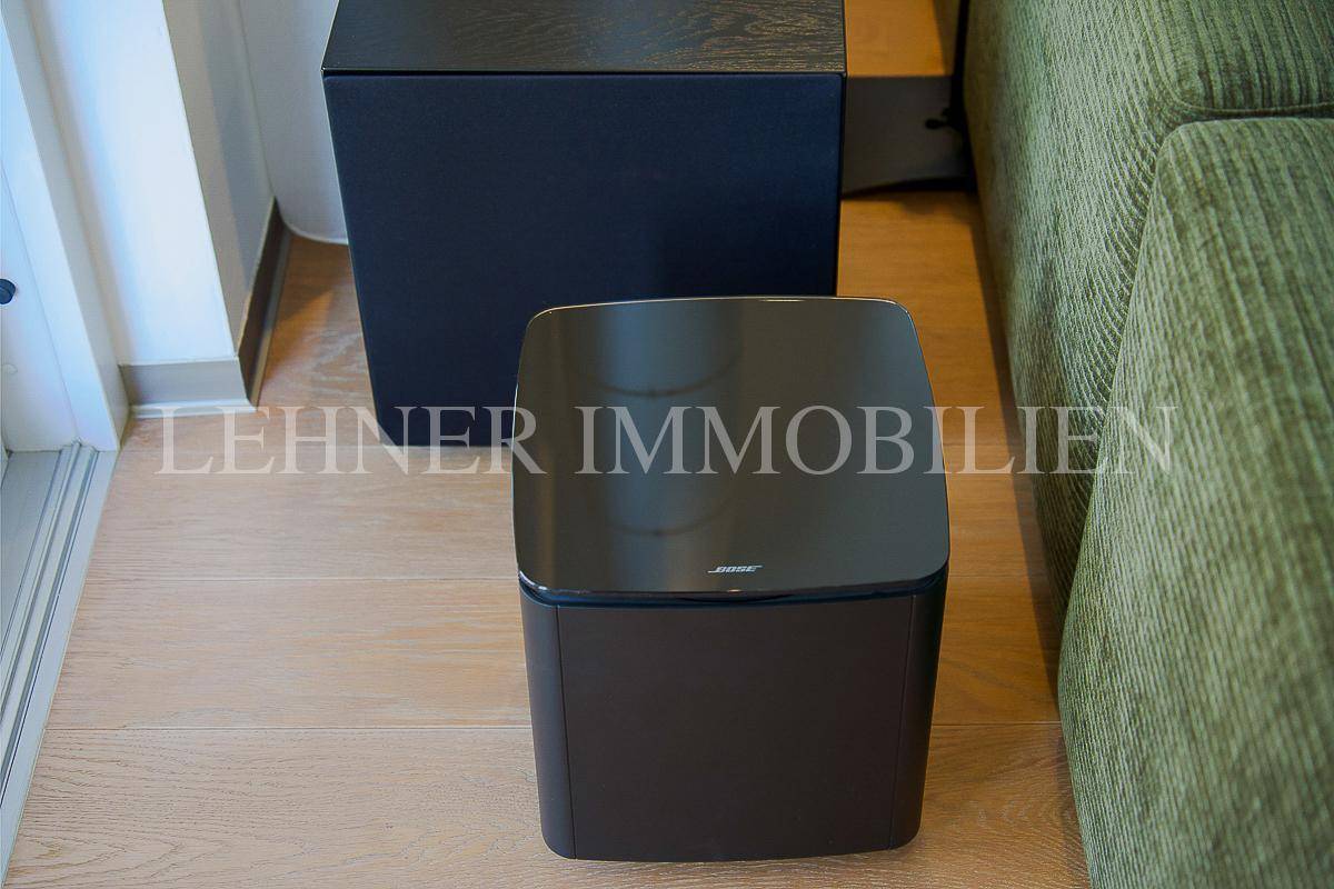 Zwei moderne schwarze Lautsprecher auf Holzfußboden neben einem grünen Sofa im Wohnzimmer.