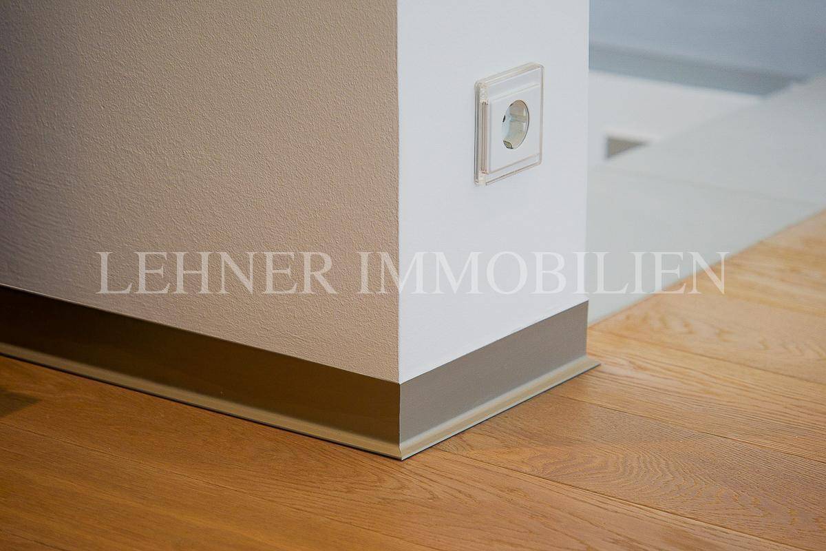 Detailansicht einer Wand mit Steckdose und Fußleiste auf einem hellen Holzfußboden.