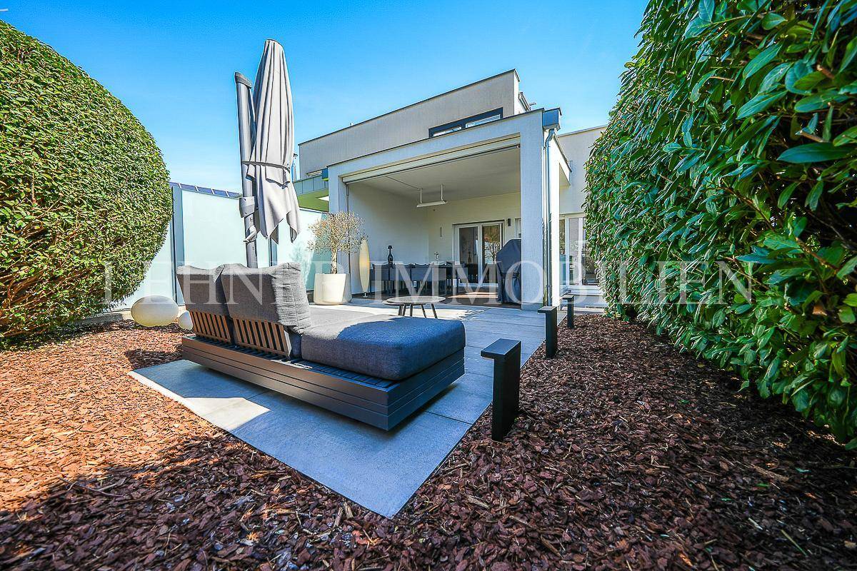 Weitläufiger Garten mit Lounge-Bereich, Mulch und Blick auf die überdachte Terrasse des Hauses.