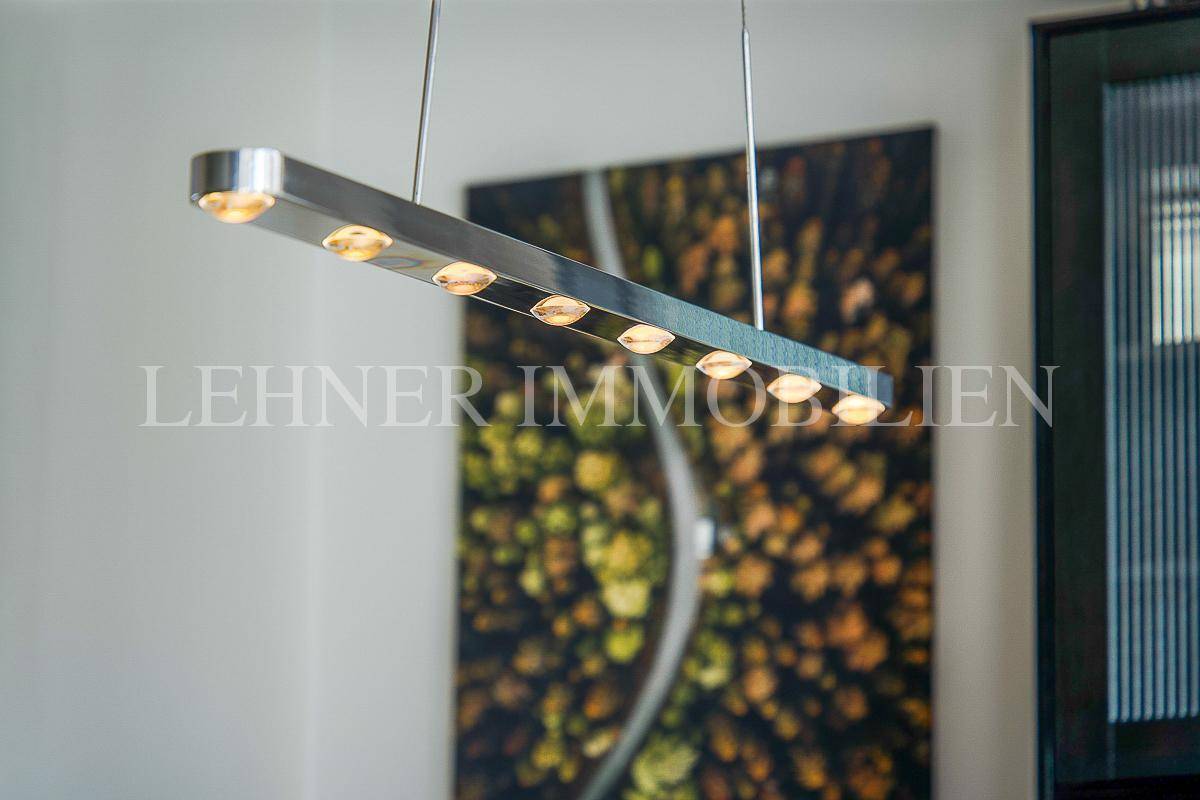 Detailaufnahme einer modernen Hängelampe über dem Essbereich mit abstraktem Kunstwerk im Hintergrund.