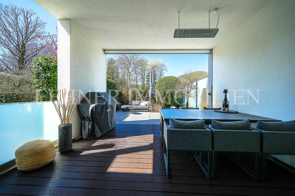 Geräumige überdachte Terrasse mit Essbereich, Grill und Lounge-Möbeln, umgeben von Natur.