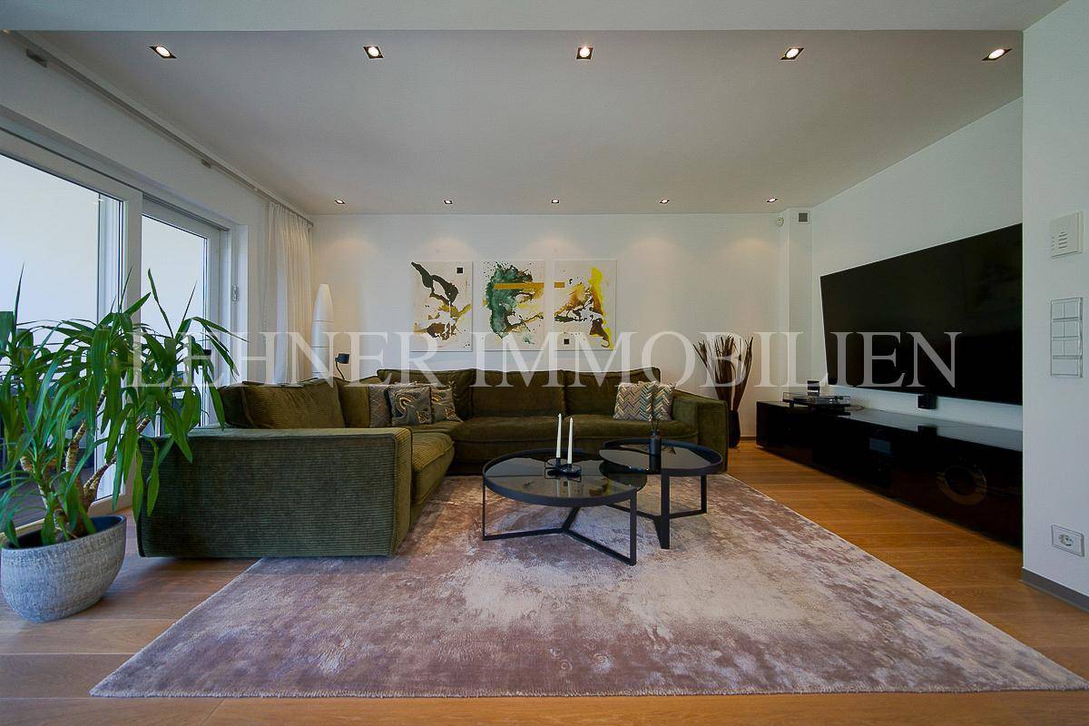 Geräumiges Wohnzimmer mit modernem Sofa, großem Fernseher und Zugang zu einem Außenbereich.