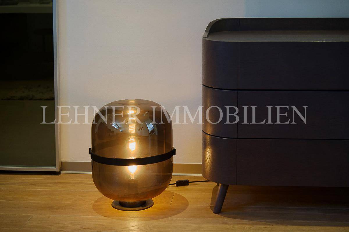 Detailaufnahme einer modernen Lampe und einer dunklen Kommode in einem stilvollen Innenraum.