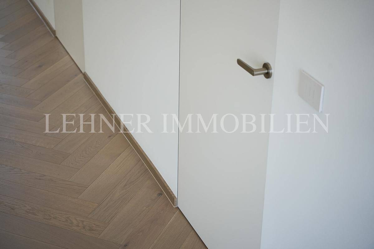 Detailansicht einer modernen Tür mit Fischgrätparkett und minimalistischer Sockelleiste.