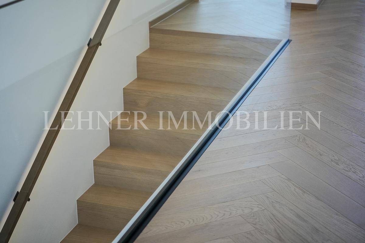 Moderne Holztreppe mit Glasgeländer und Fischgrätparkett im Treppenhaus.