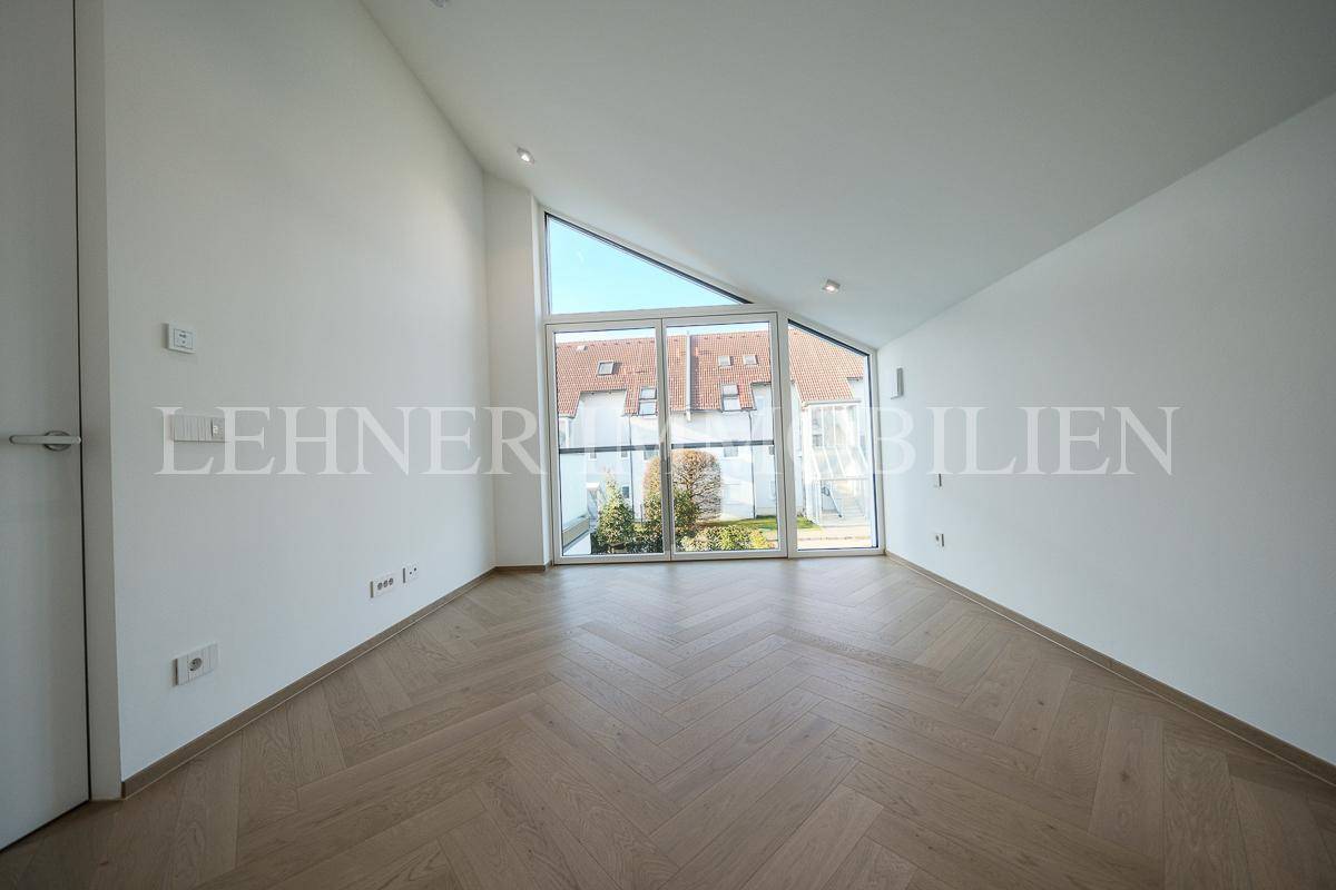 Heller Raum mit großen Fenstern, Fischgrätparkett und schräger Decke, bietet viel Tageslicht.