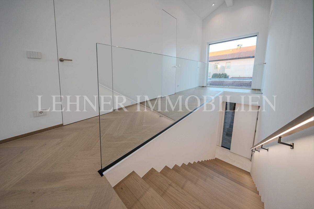 Heller Flur mit moderner Holztreppe, Glasgeländer und Blick nach draußen.