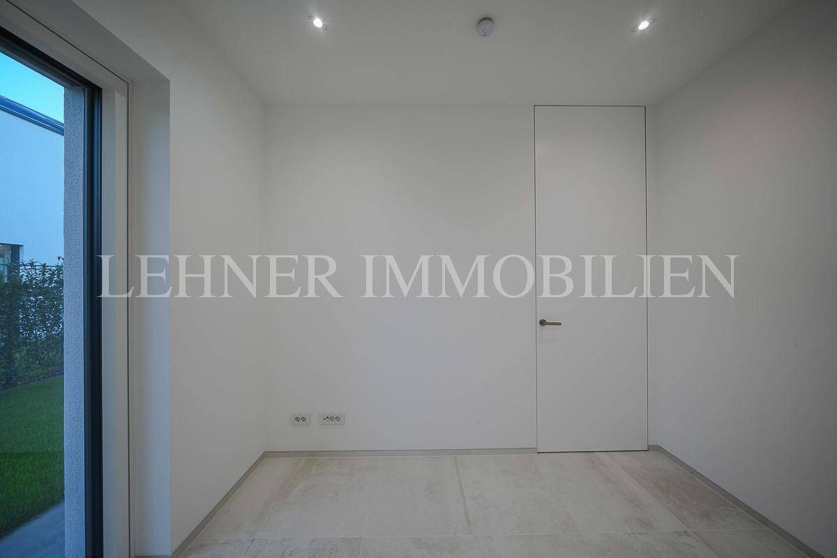 Modernes Zimmer mit Fliesenboden, großer Fenstertür und schlichter weißer Tür.