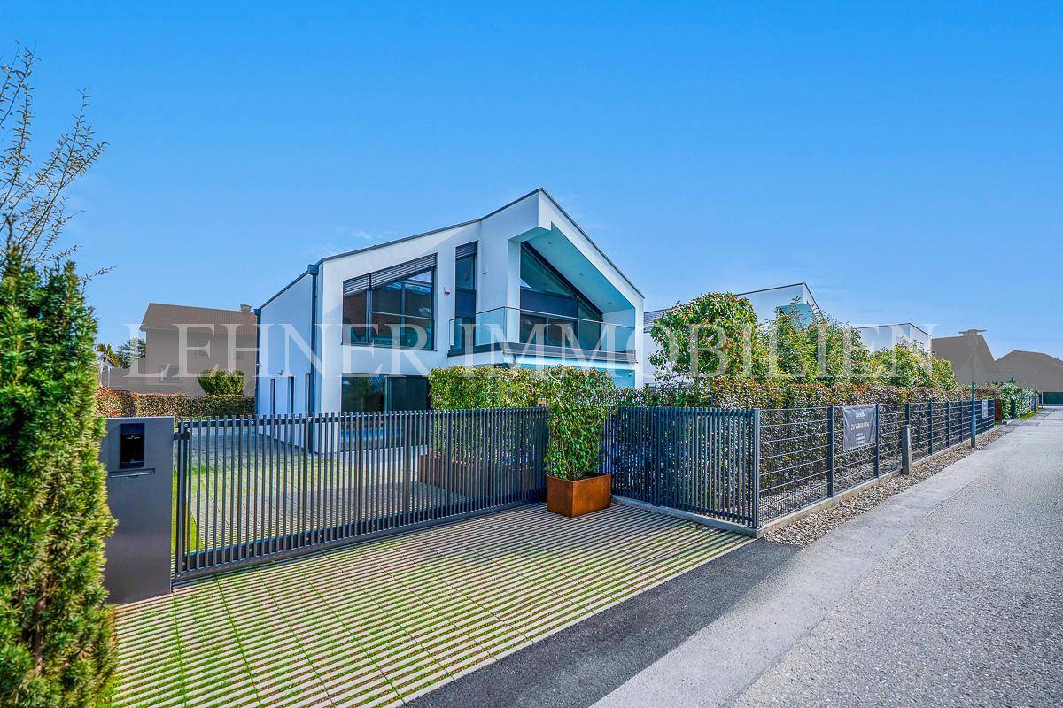 Zufahrt zur modernen Villa mit elegantem Zaun und Tor, umgeben von gepflegter Hecke.