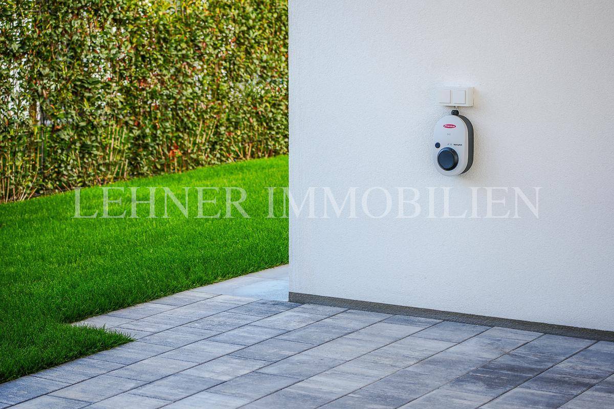Ladestation für Elektrofahrzeuge an der Hauswand, neben gepflegtem Rasen und Terrasse.