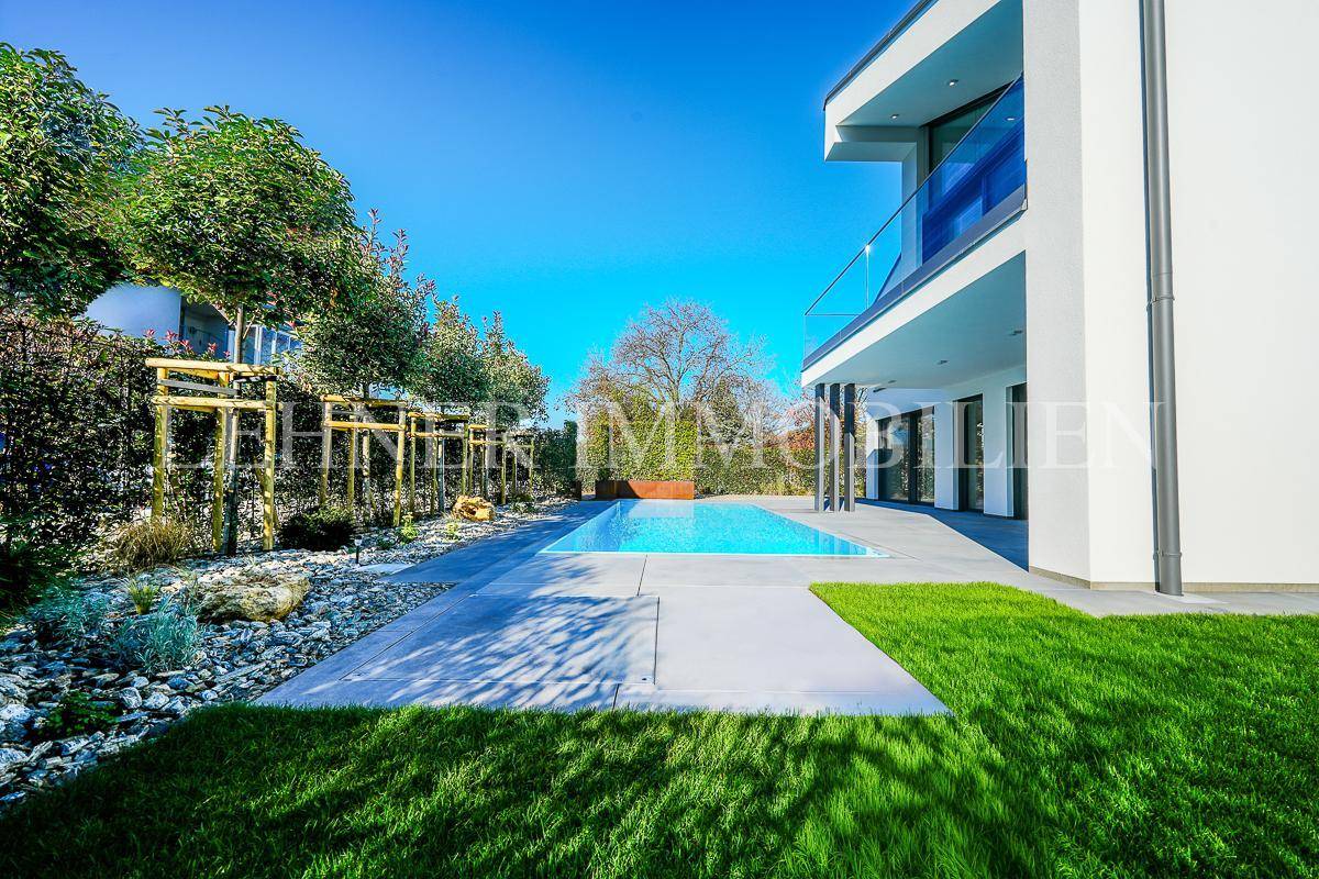 Gepflegter Gartenbereich mit Pool, Rasen und dekorativen Pflanzen unter blauem Himmel.